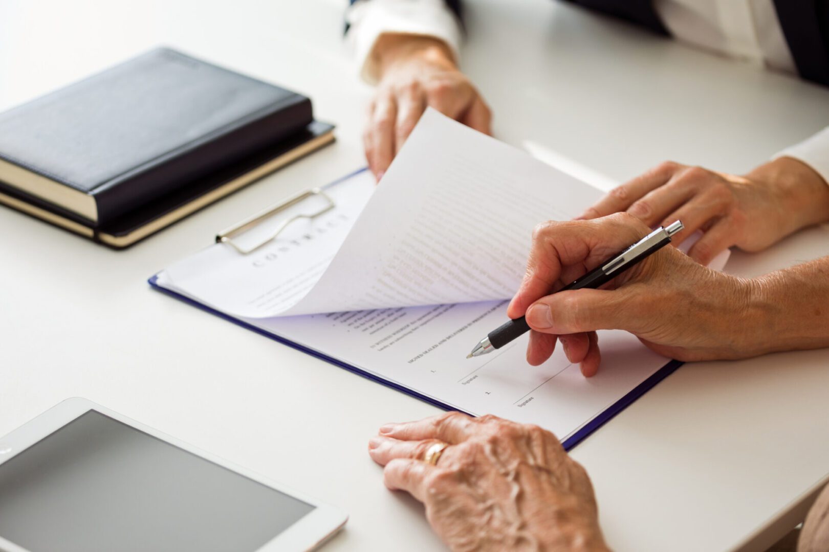 Hands signing a document on a clipboard.
