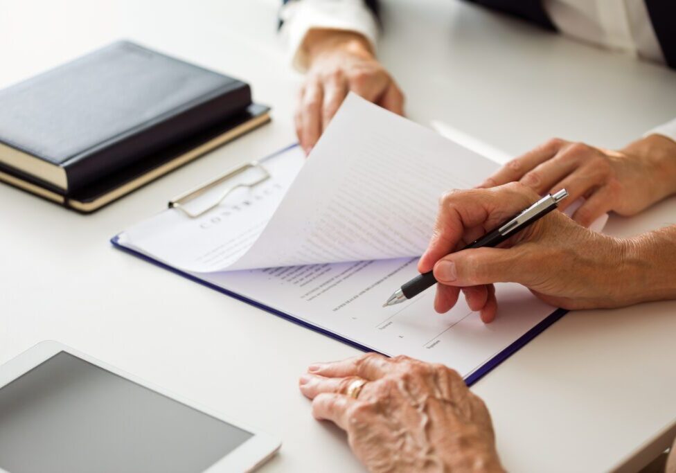 Hands signing a document on a clipboard.